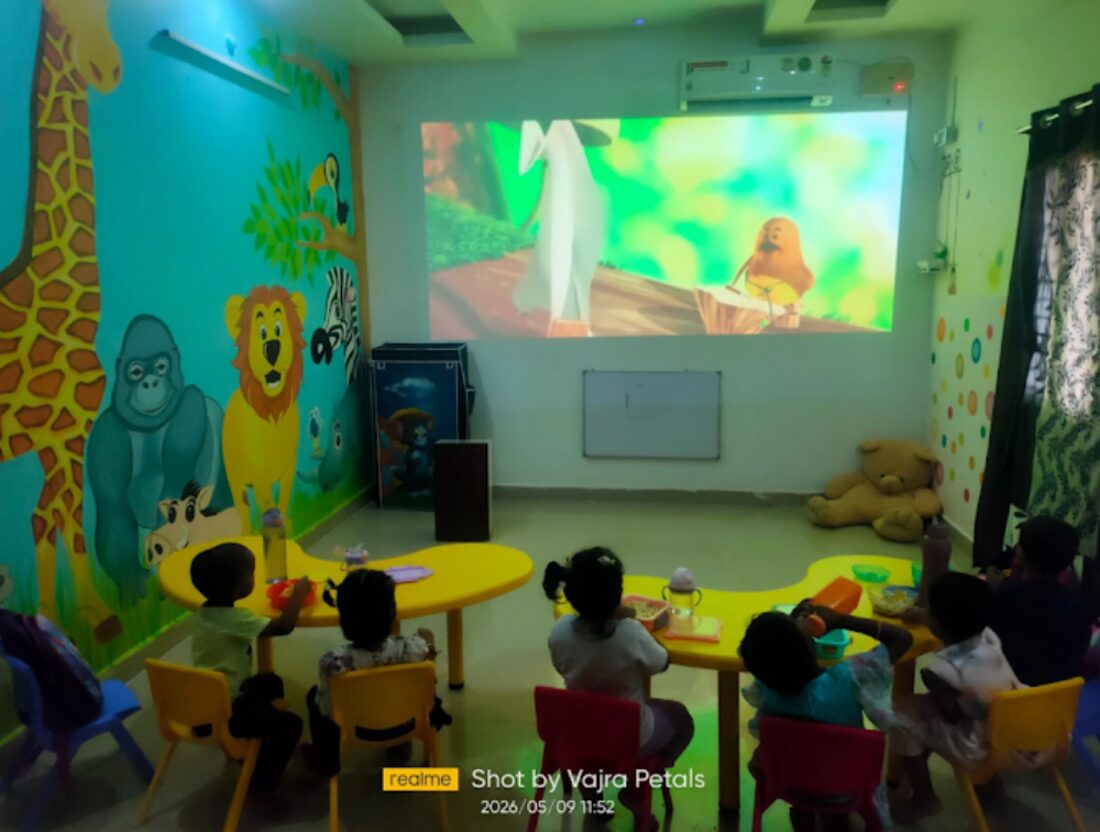 Children seated at a table watching an animated story on a projector screen in a jungle-themed classroom